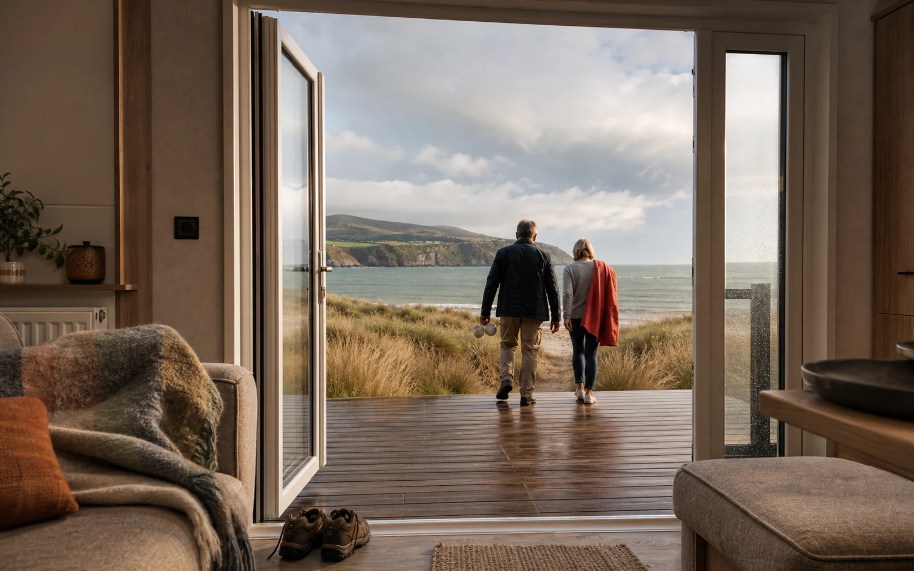 A couple step through the open doors of their holiday home towards a North Wales beach